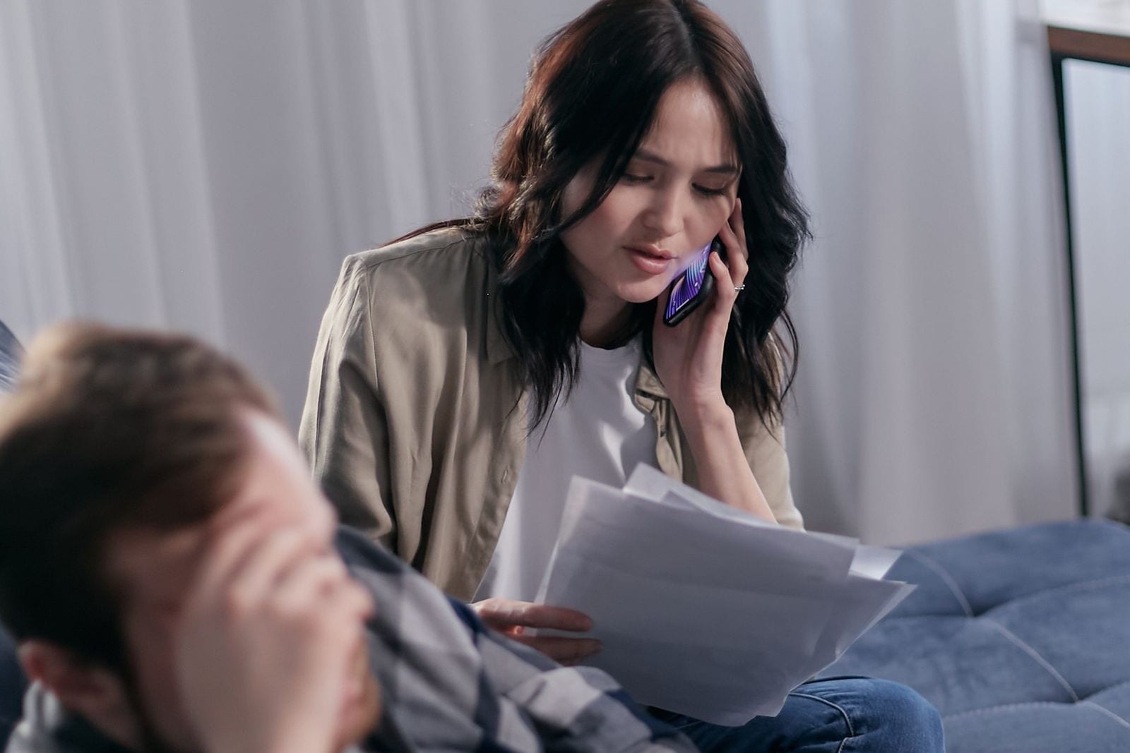 A worried couple reviewing paperwork while one person makes a telephone call.